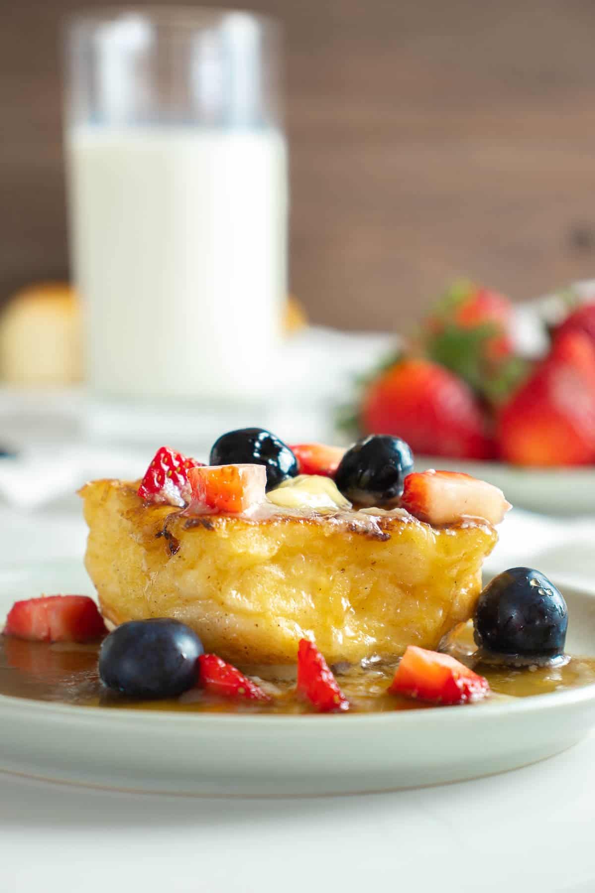 Close up of Hawaiian roll french toast on plate with butter, syrup and berries.