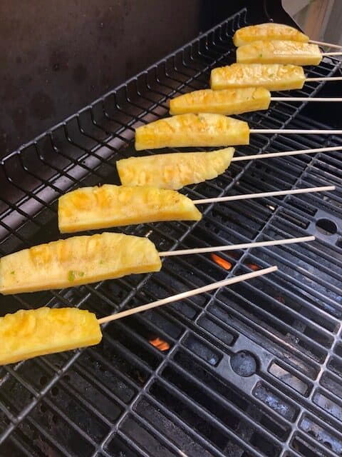 Grilled pineapple on skewers on BBQ.