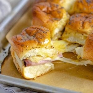 Baked ham and cheese sliders on a sheet pan being pulled apart.