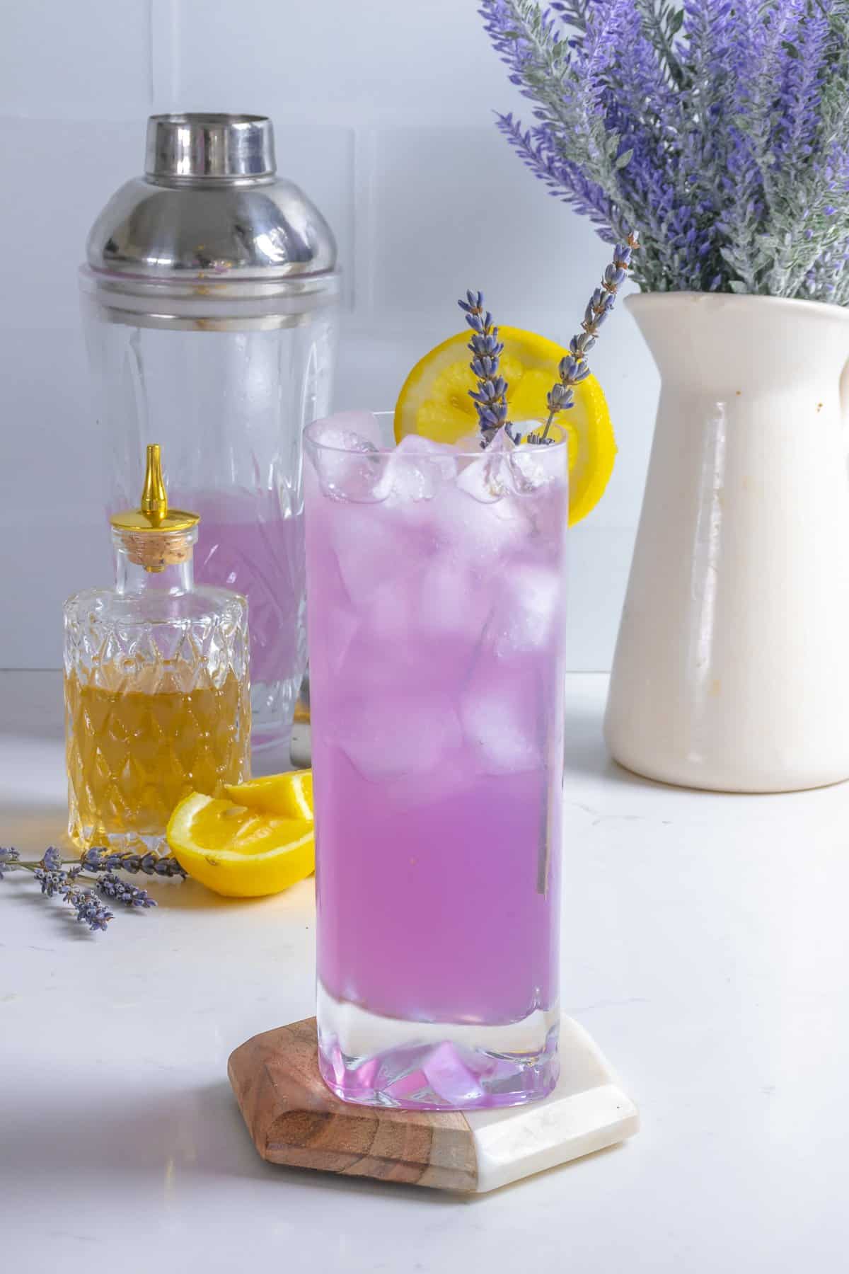 Lavender lemonade with syrup and shaker on table.