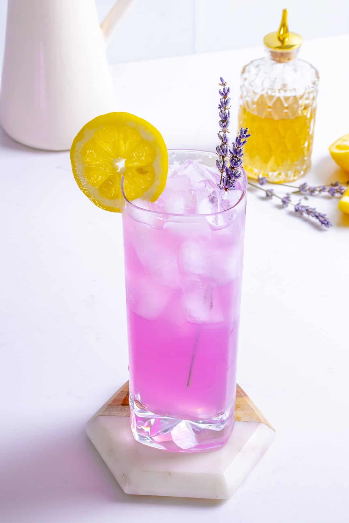 Lavender lemonade on table with lemon and flowers.
