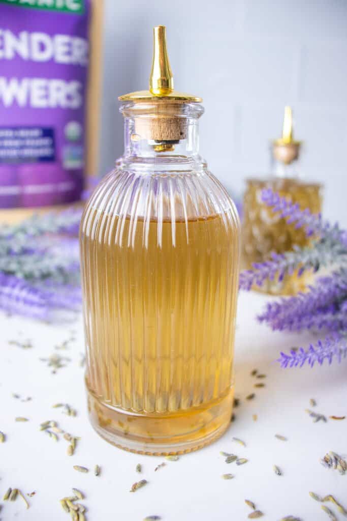 Bottle of lavender simple syrup on table with dried lavender buds.