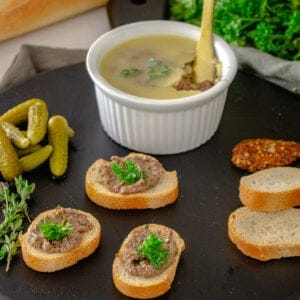 Chicken liver pate in a ramekin on cutting board with crostini.