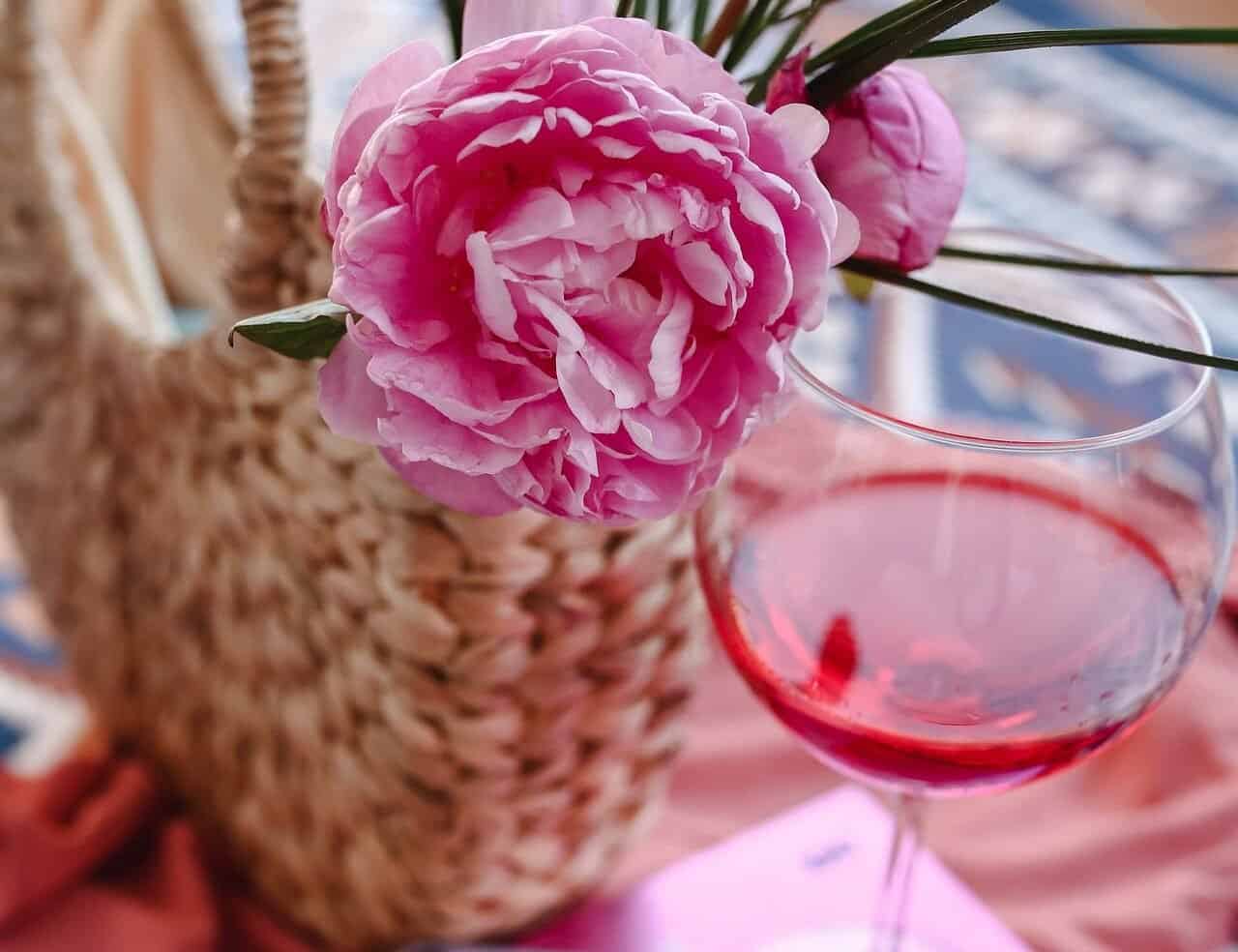 Pink peony flower in a basket next to a wine glass.