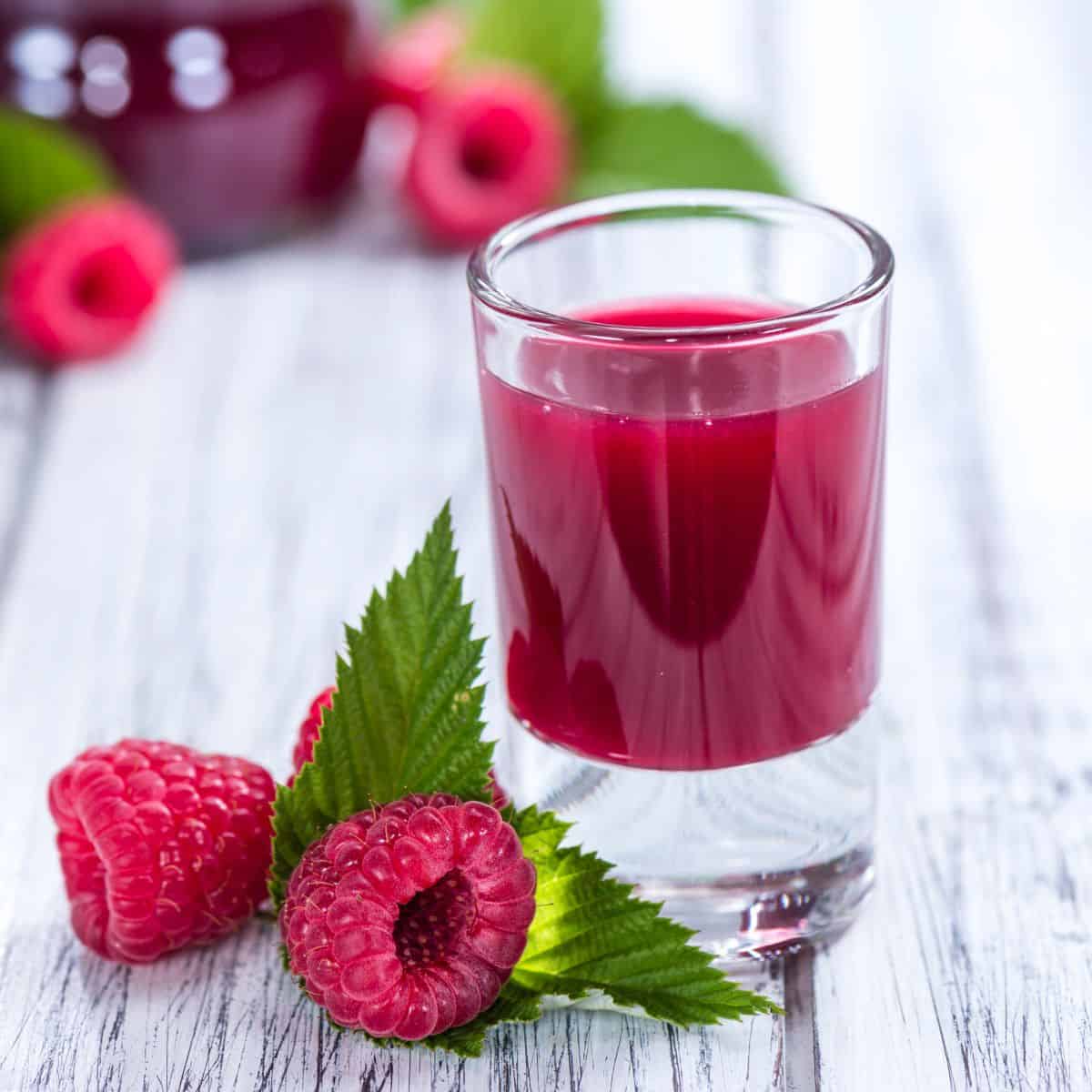 Black raspberry liqueur in a shot glass with raspberries around it.
