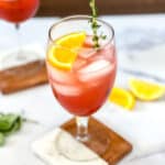 Aperol spritz mocktail on table with citrus and herbs.