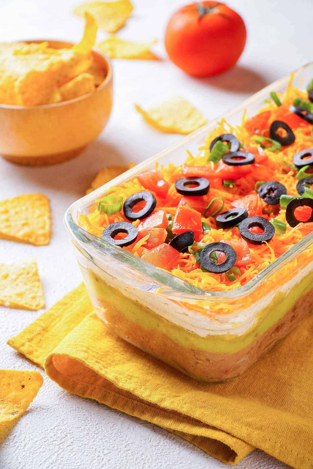 Seven layer taco dip with tortilla chips on a table on yellow napkin.