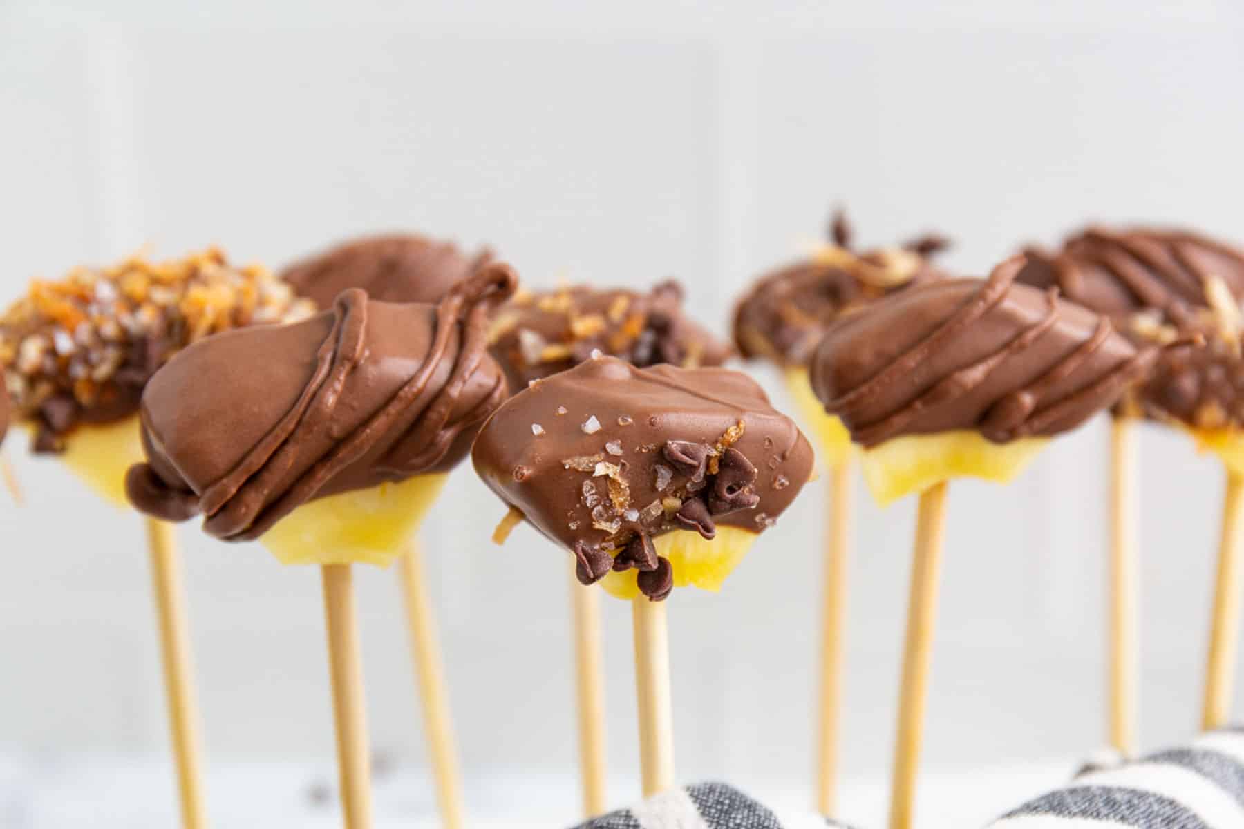 Chocolate dipped pineapple skewers with coconut standing upright.