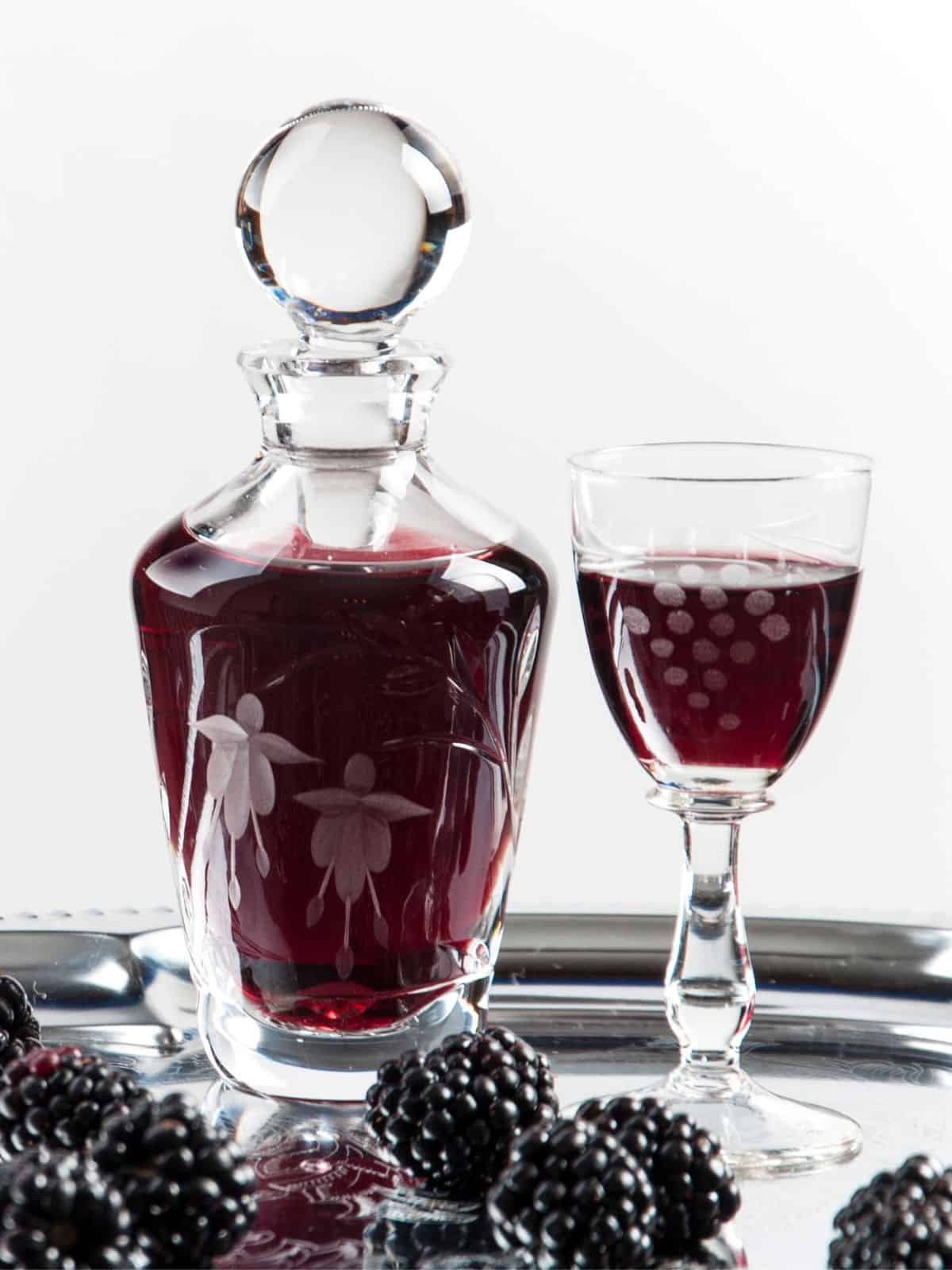 A dark red colored cordial in a decanter and glass.