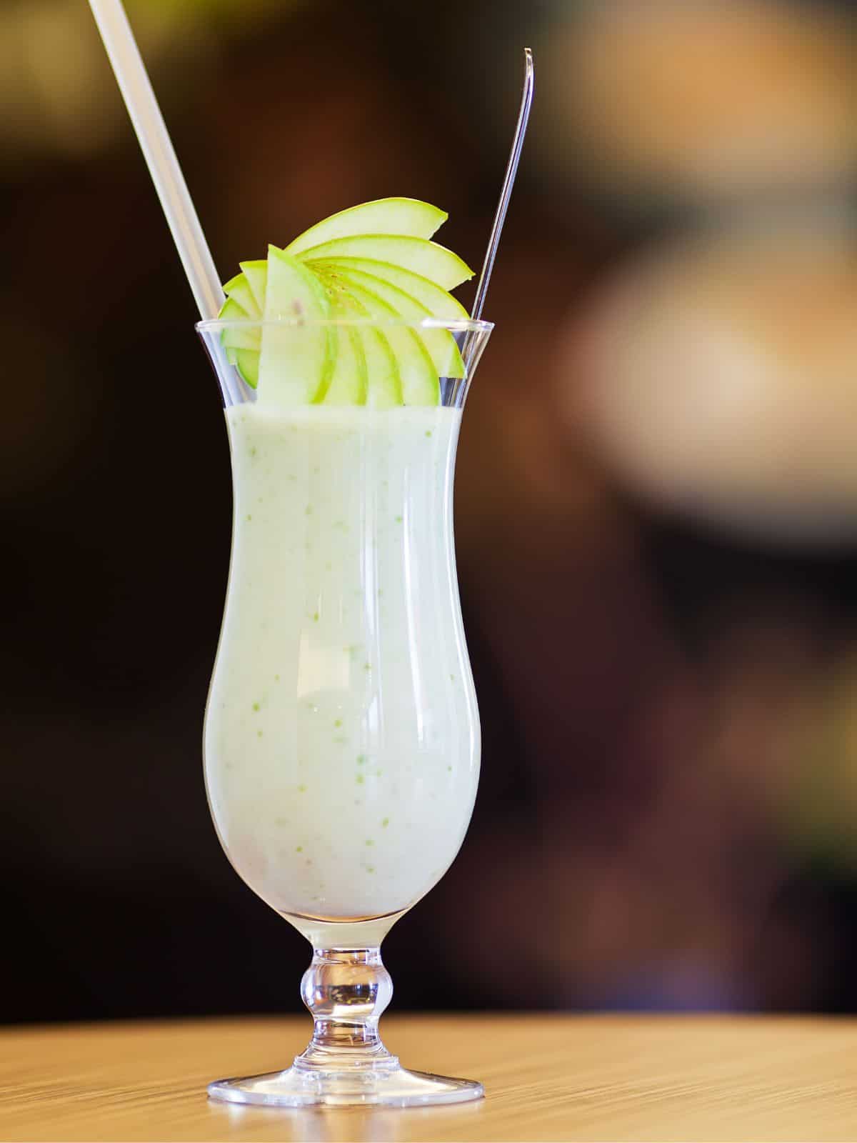 A hurricane glass with white cocktail and sliced pears garnish.