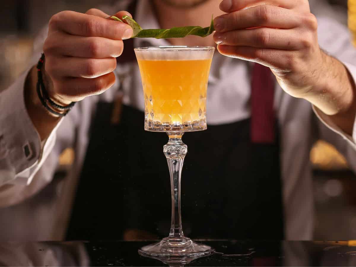 A bartender adding a garnish to a cocktail in a sour glass.