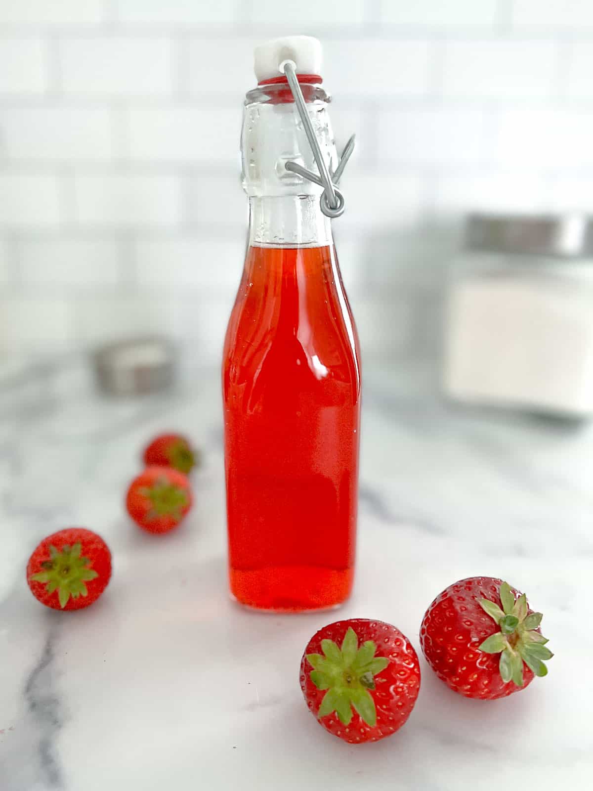 Homemade strawberry simple syrup in a glass bottle with strawberries on ground.

