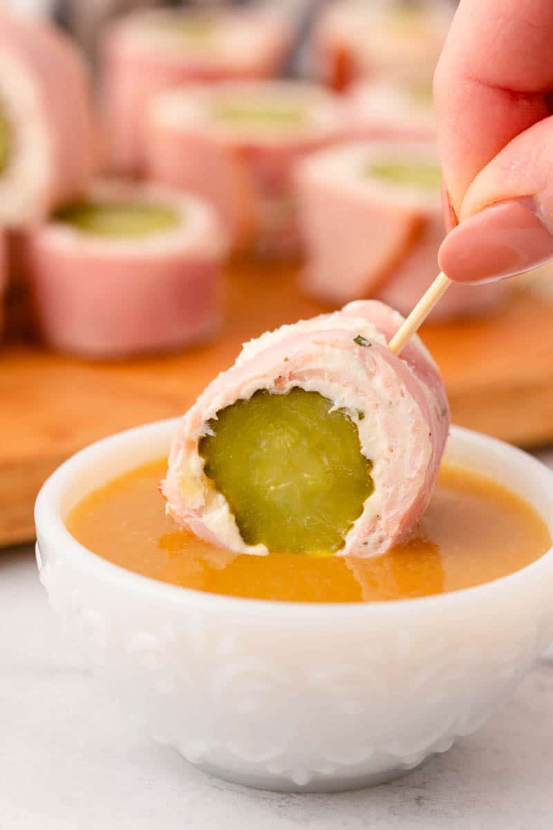 Dipping pickle roll up in honey mustard sauce.