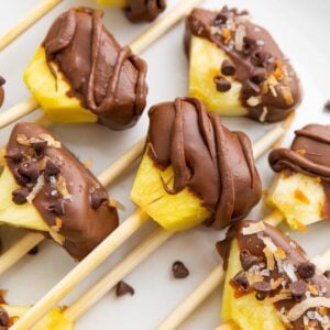 Pineapple skewers covered in chocolate and coconut and skewered.
