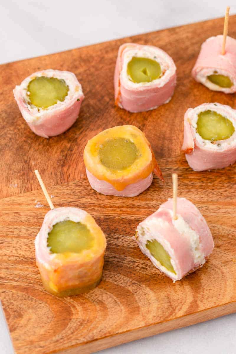 Pickle and ham roll ups on a cutting board with toothpicks.