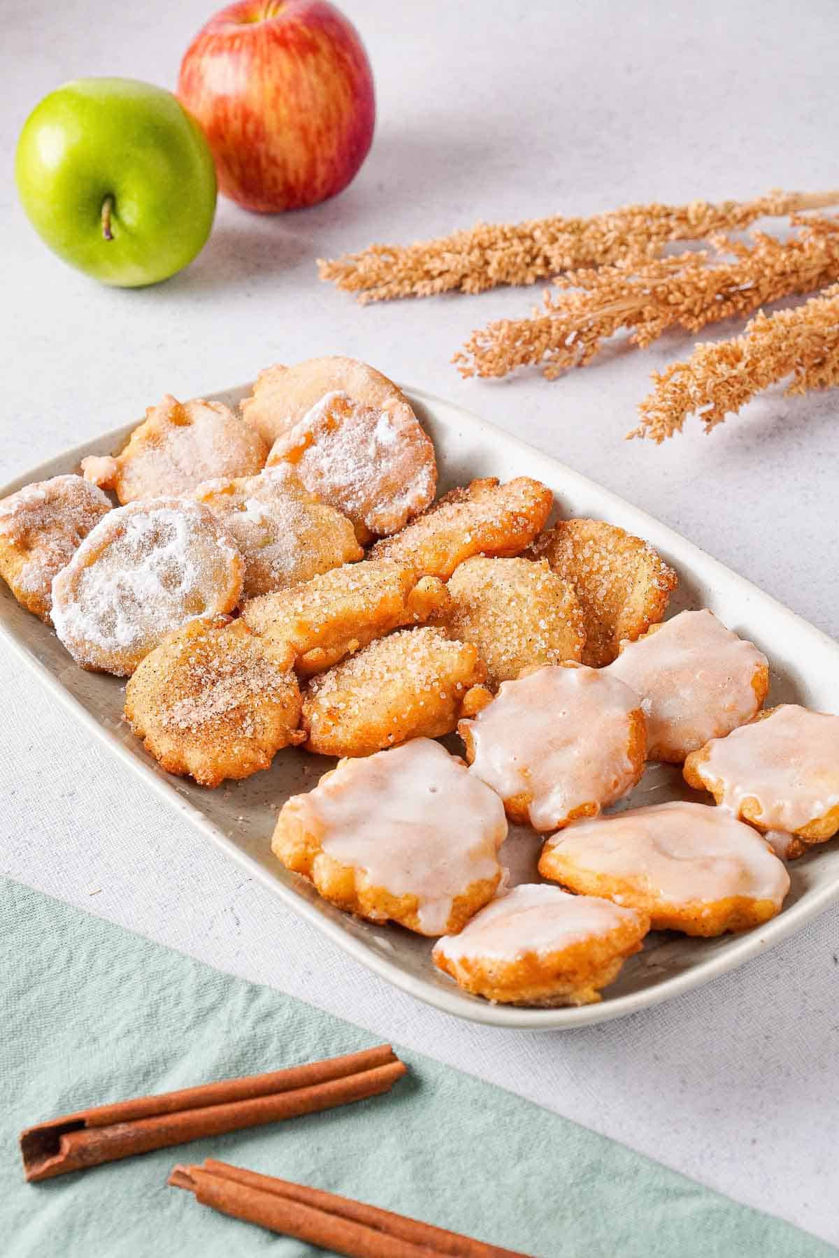 Apple pie fritters on a plate covered in powdered sugar, glaze and cinnamon sugar.