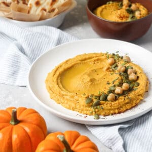 Pumpkin hummus on white plate with chick peas.