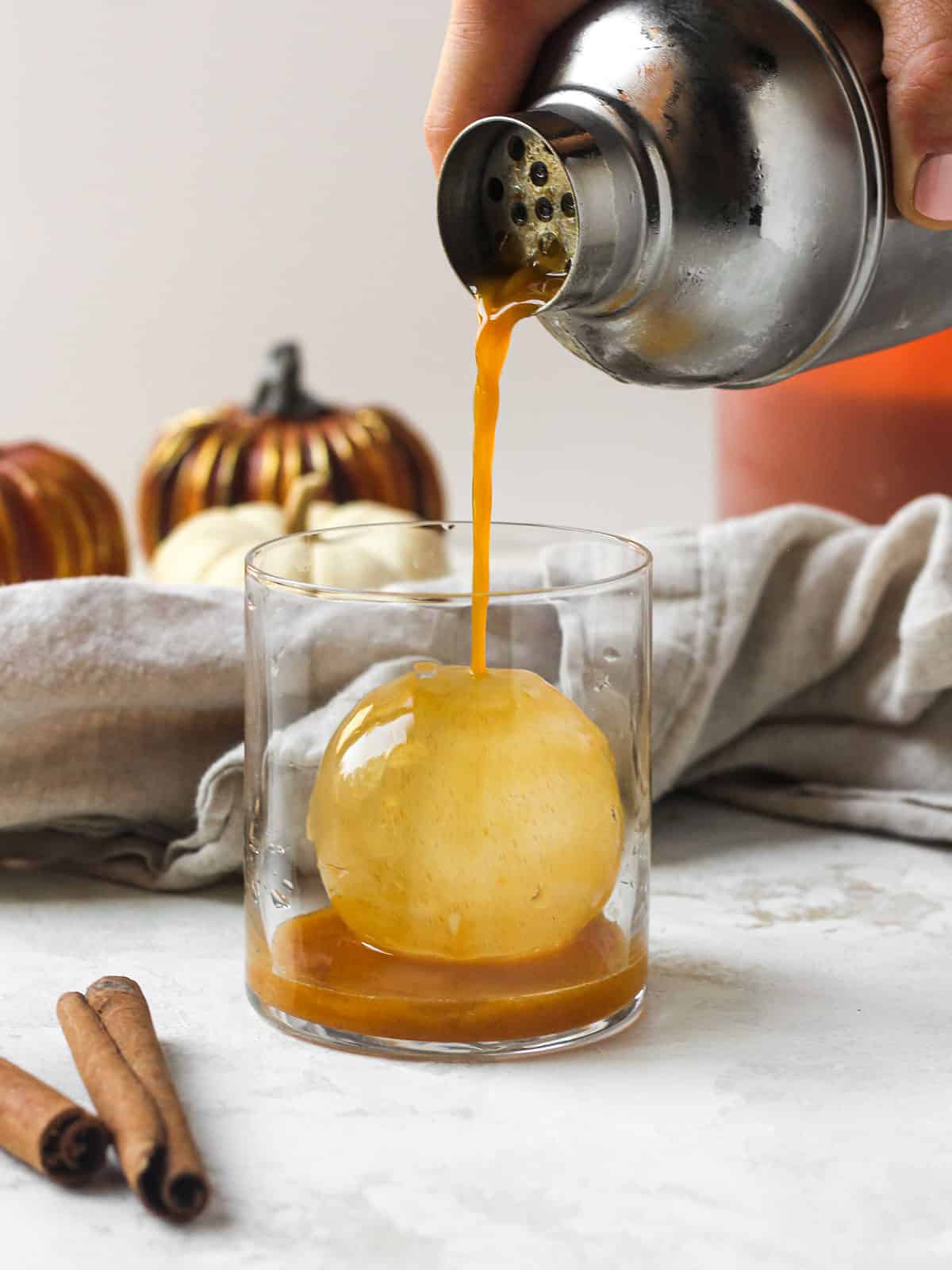 Bourbon Fall cocktail being poured into whiskey glass on ice ball.