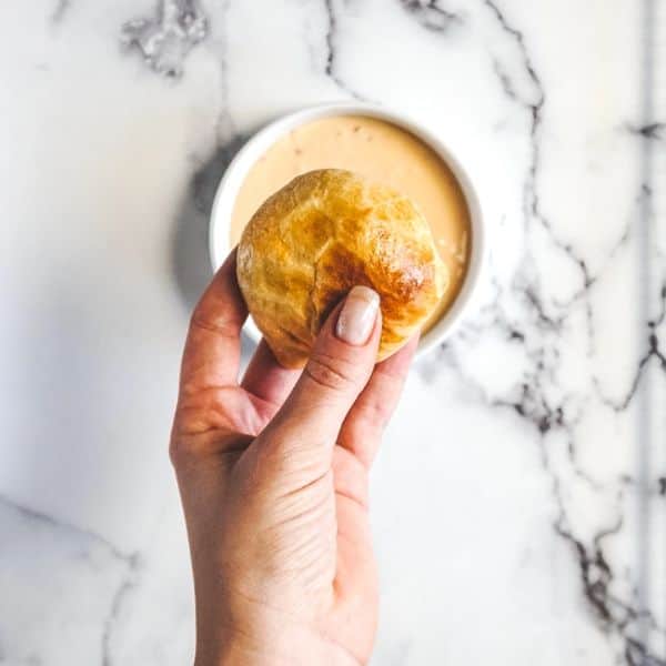hand holding a buffalo chicken bite over a bowl of sauce.
