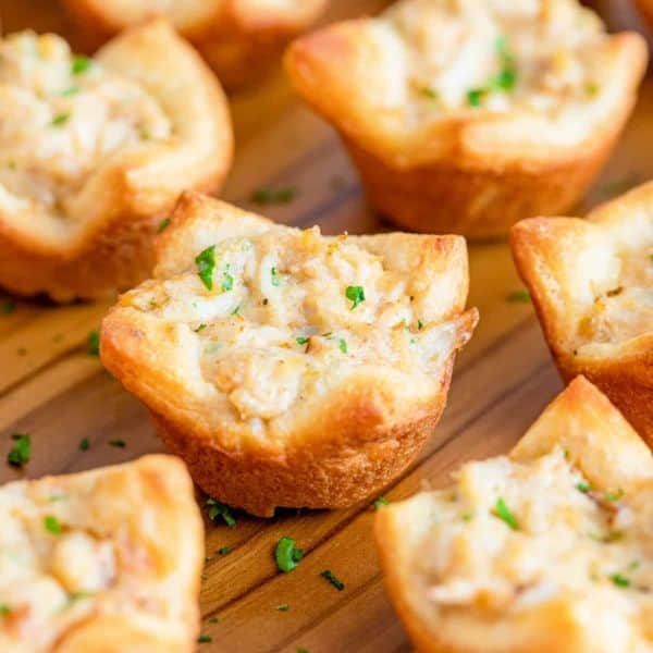 crescent roll crab puffs on a wooden cutting board topped with herbs.