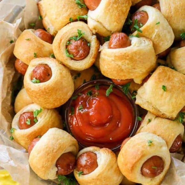 mini pigs in a blanket surrounding a bowl of ketchup.