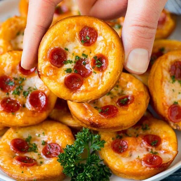 mini pizzas with pepperoni being picked up by two fingers.
