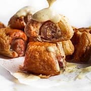 Puff pastry pigs in a blanket with sauce spooned over top.