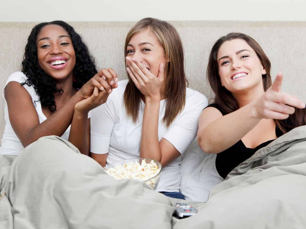 Women sitting on couch watching a movie with popcorn.