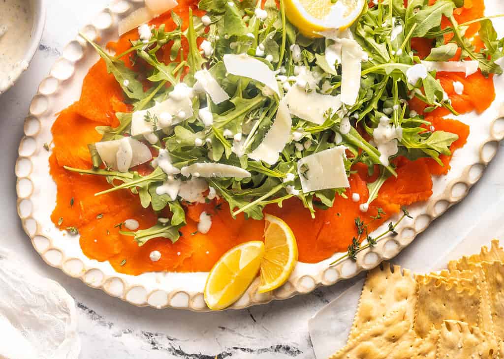 Smoked salmon carpaccio with arugula and parmesan on plate.