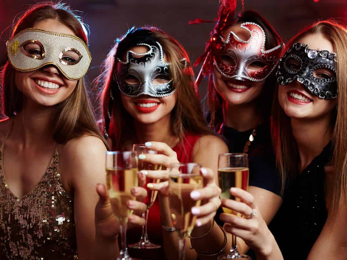 Women celebrating at a masquerade party with drinks.