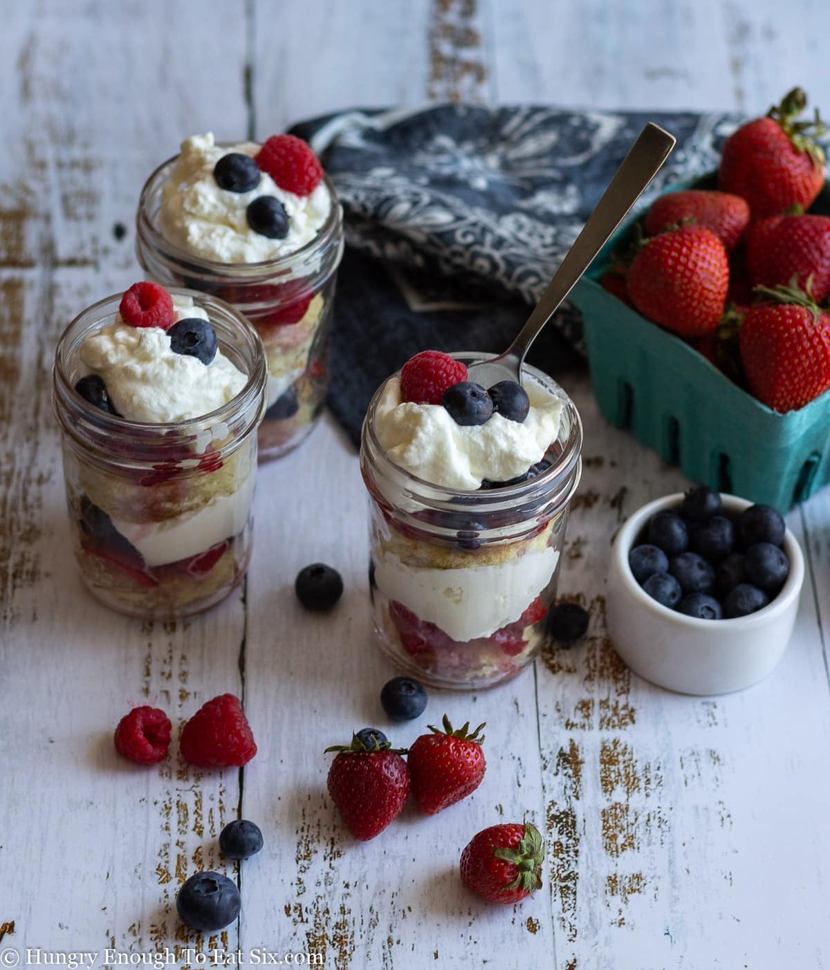 3 triple berry mason jar dessert cups with fresh strawberries, blueberries and whipped cream.