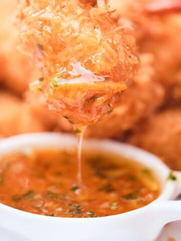 Coconut shrimp being dipped into a sauce.