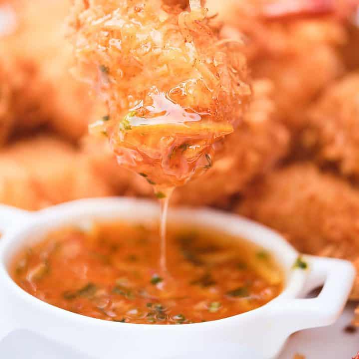 Coconut shrimp being dipped into a sauce.