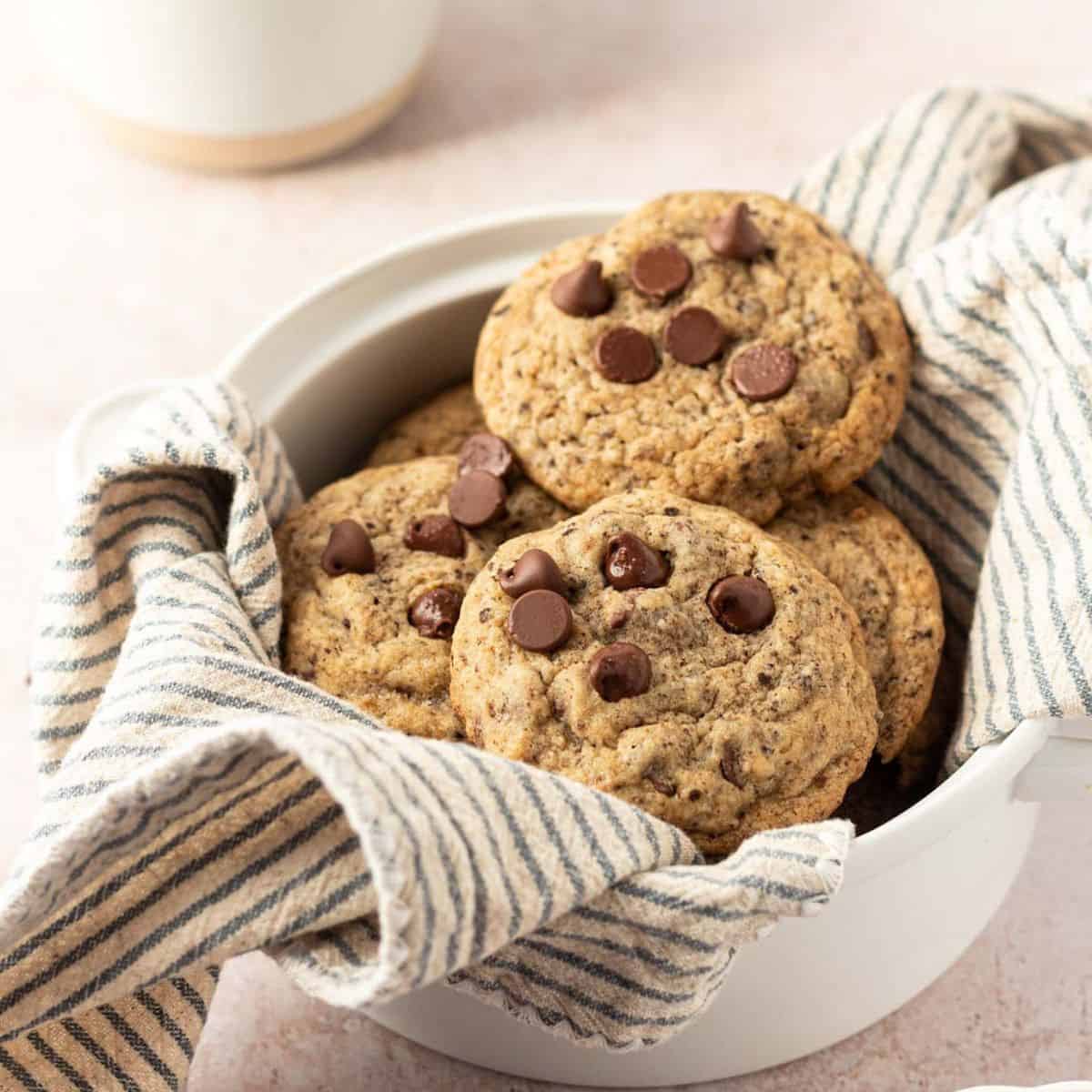 Espresso chocolate chip cookies in a bowl with a dishtowel and a cup of espresso on the side.