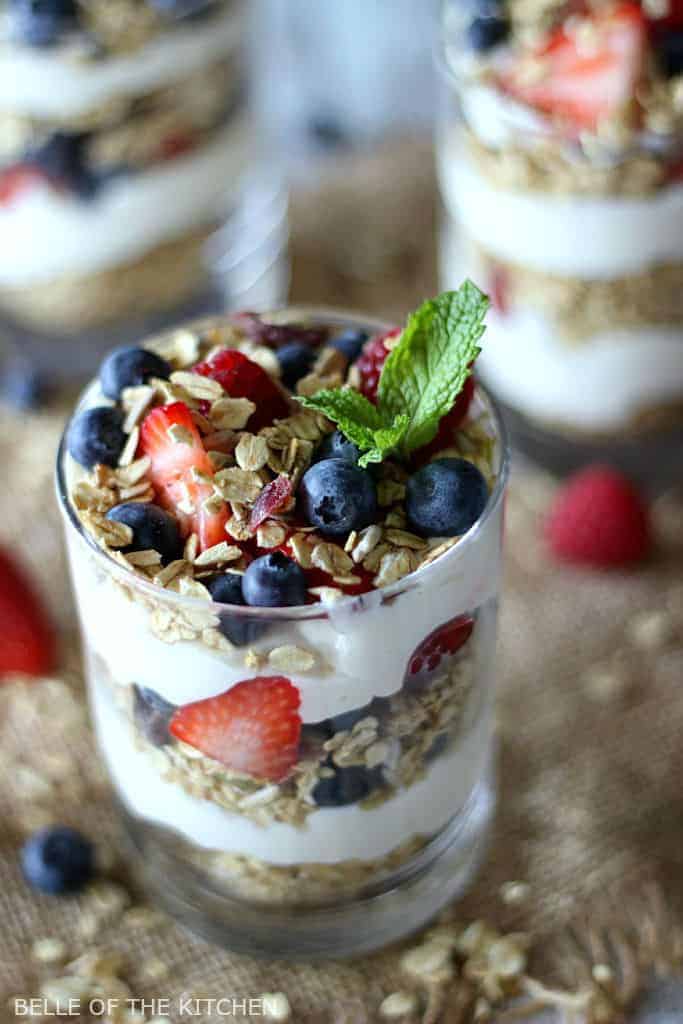 greek yogurt cheesecake parfait with strawberries and blueberries, topped with mint leaves and granola.