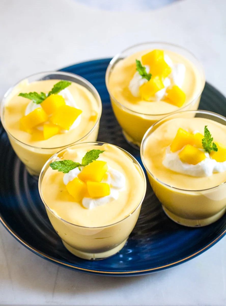 4 mango mousse dessert cups on a blue plate with fresh mango and mint leaves.