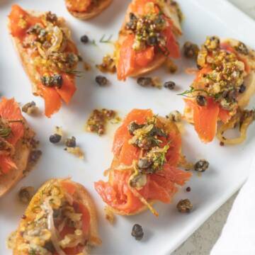 Smoked salmon crostini appetizer with capers and dill on plate.