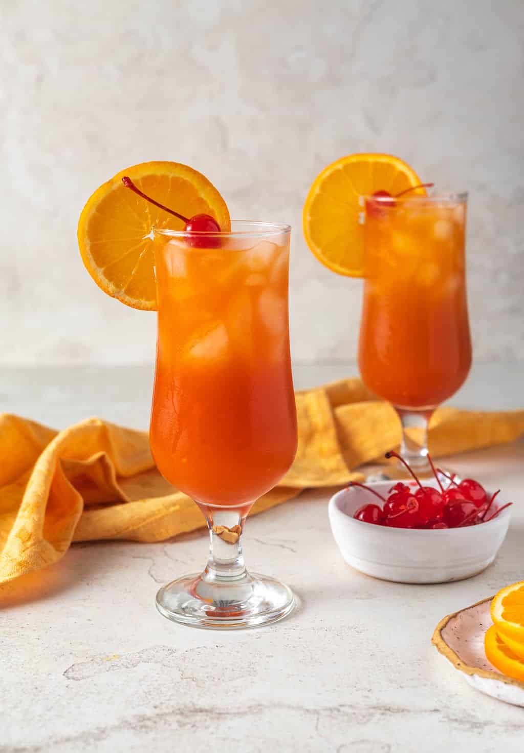 Hurricane cocktail on table with orange and cherries.