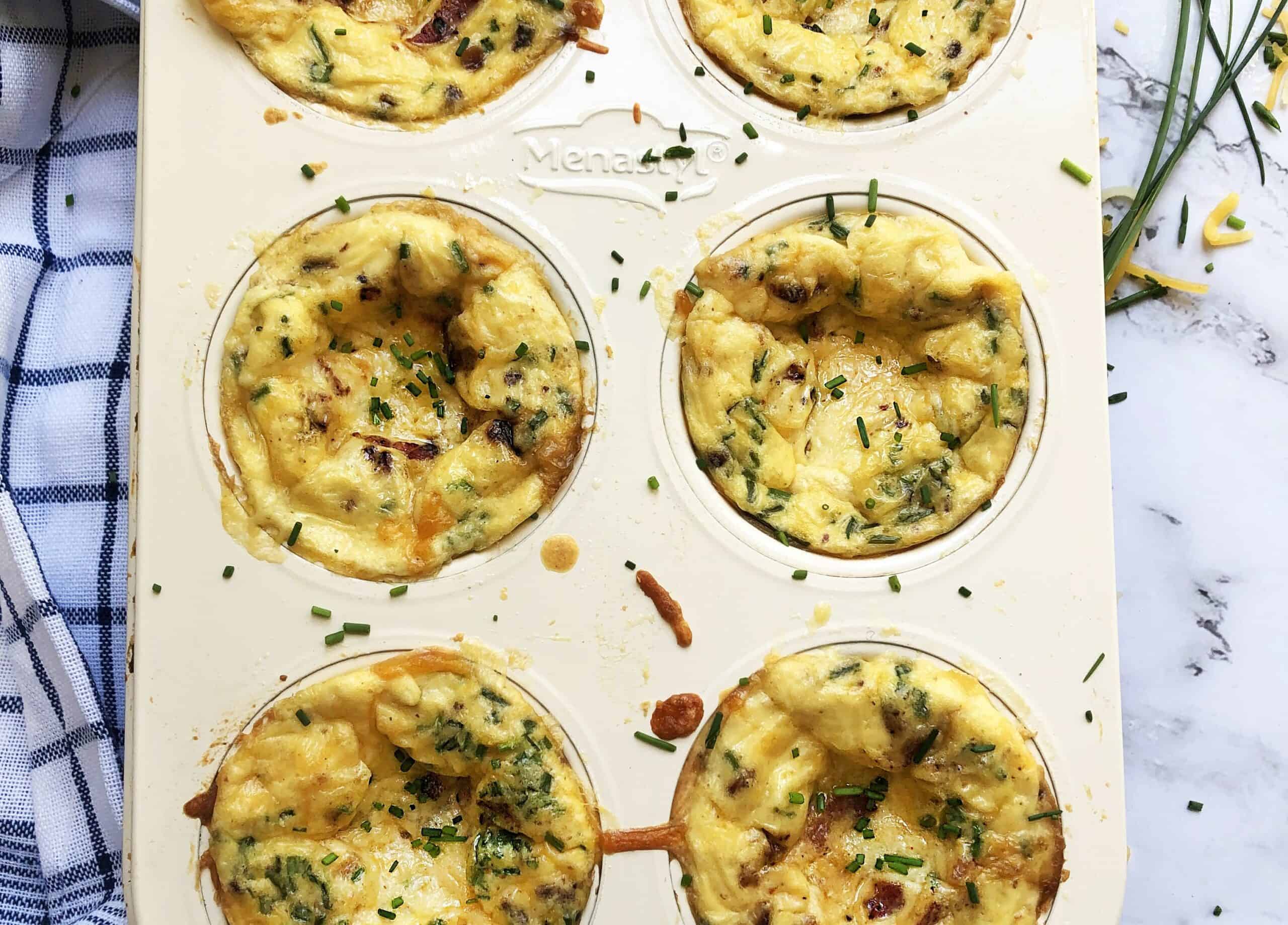 Baked egg bites in a muffin tin topped with melted cheese and bacon.