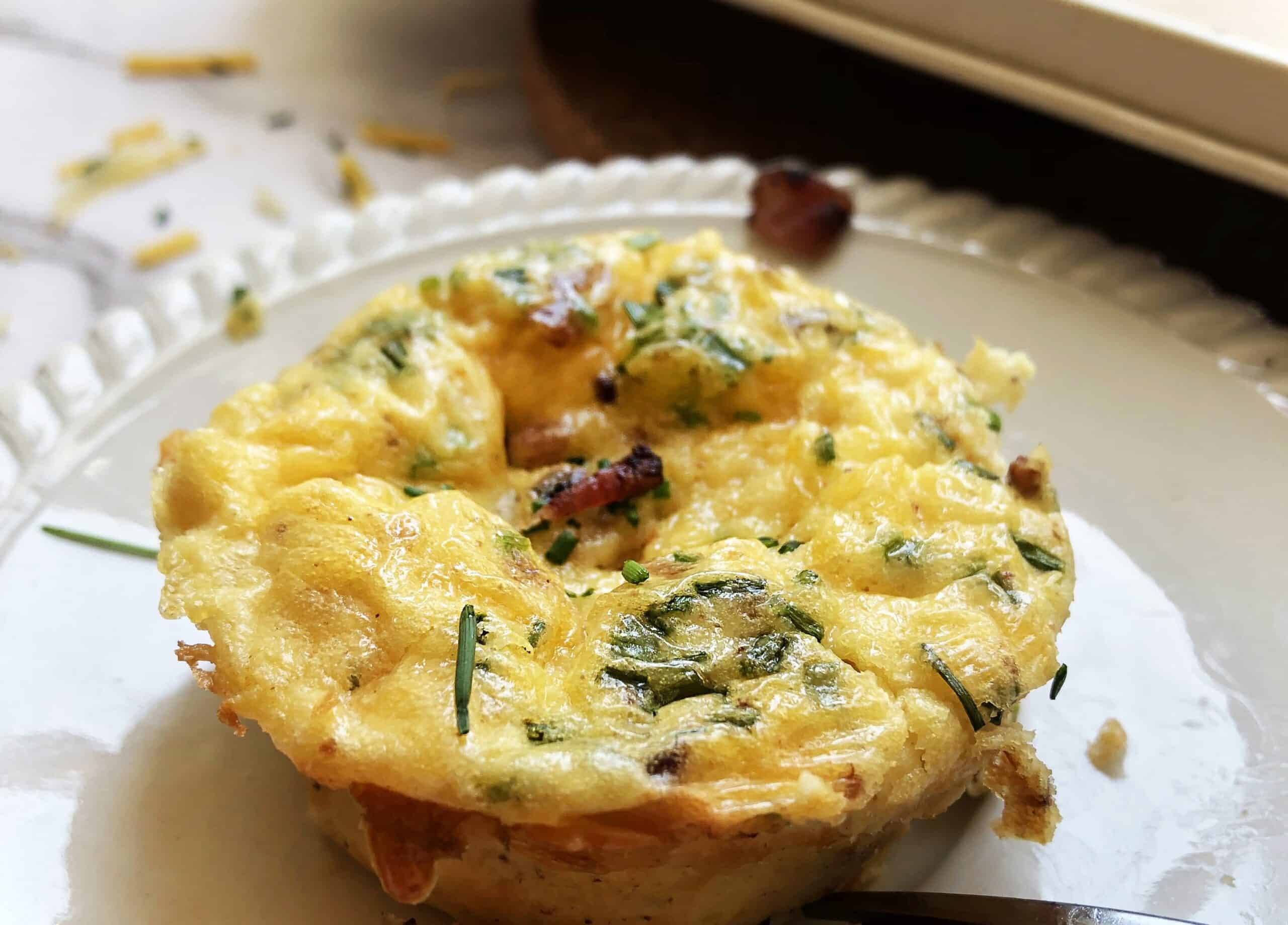 Cheesy egg bites plated with fork and crumbled bacon on top.