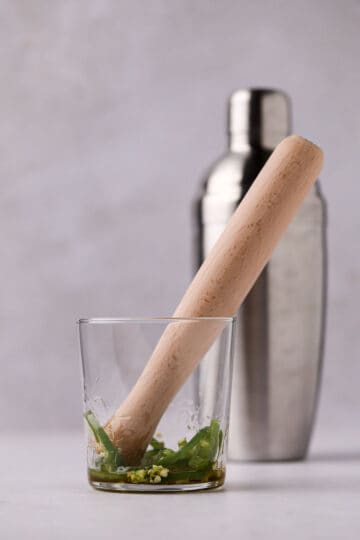 Glass with ingredients and cocktail shaker.
