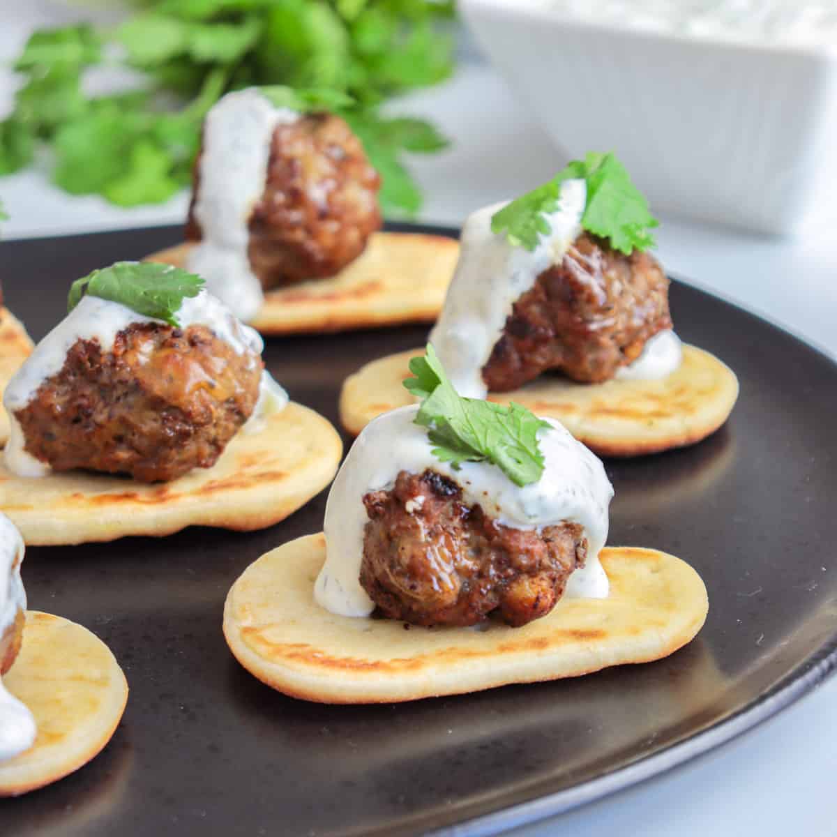 Lamb meatballs on top of naan with a drizzle of yogurt sauce.