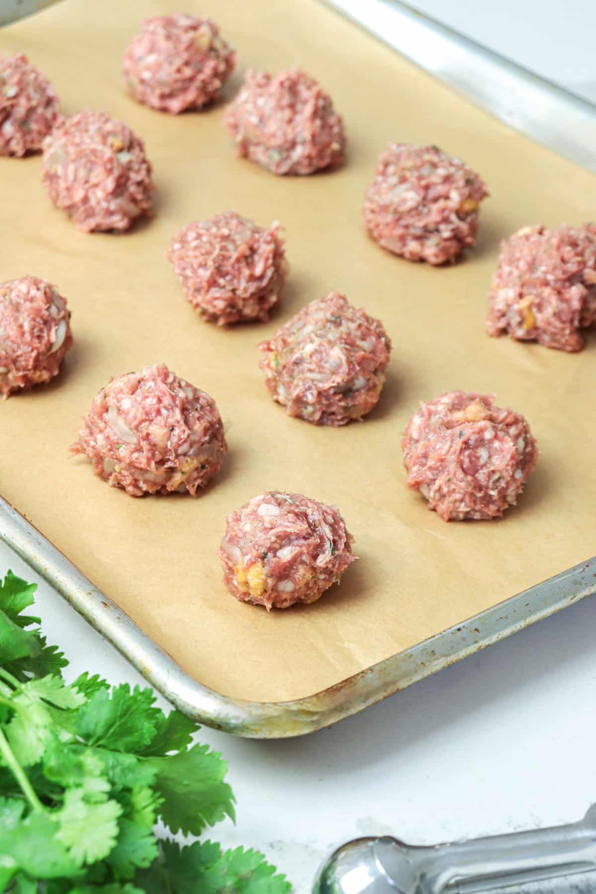 Raw lamb meatballs shaped into balls on a baking sheet.