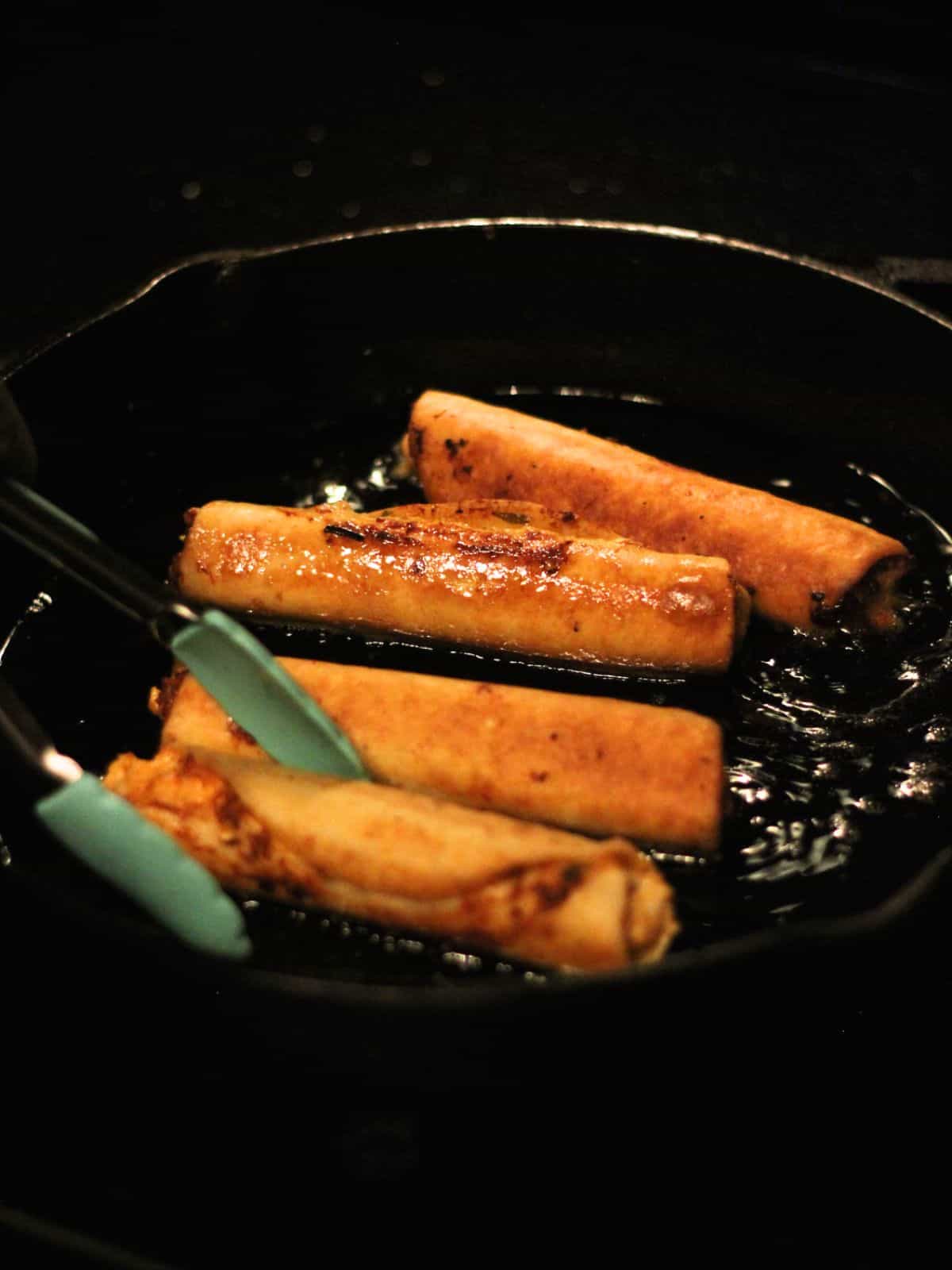 Frying chicken flautas in cast iron pan.