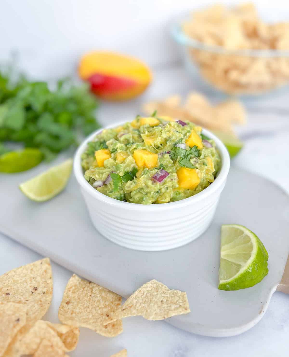 Mango guacamole in a bowl with lime wedge and tortilla chips.