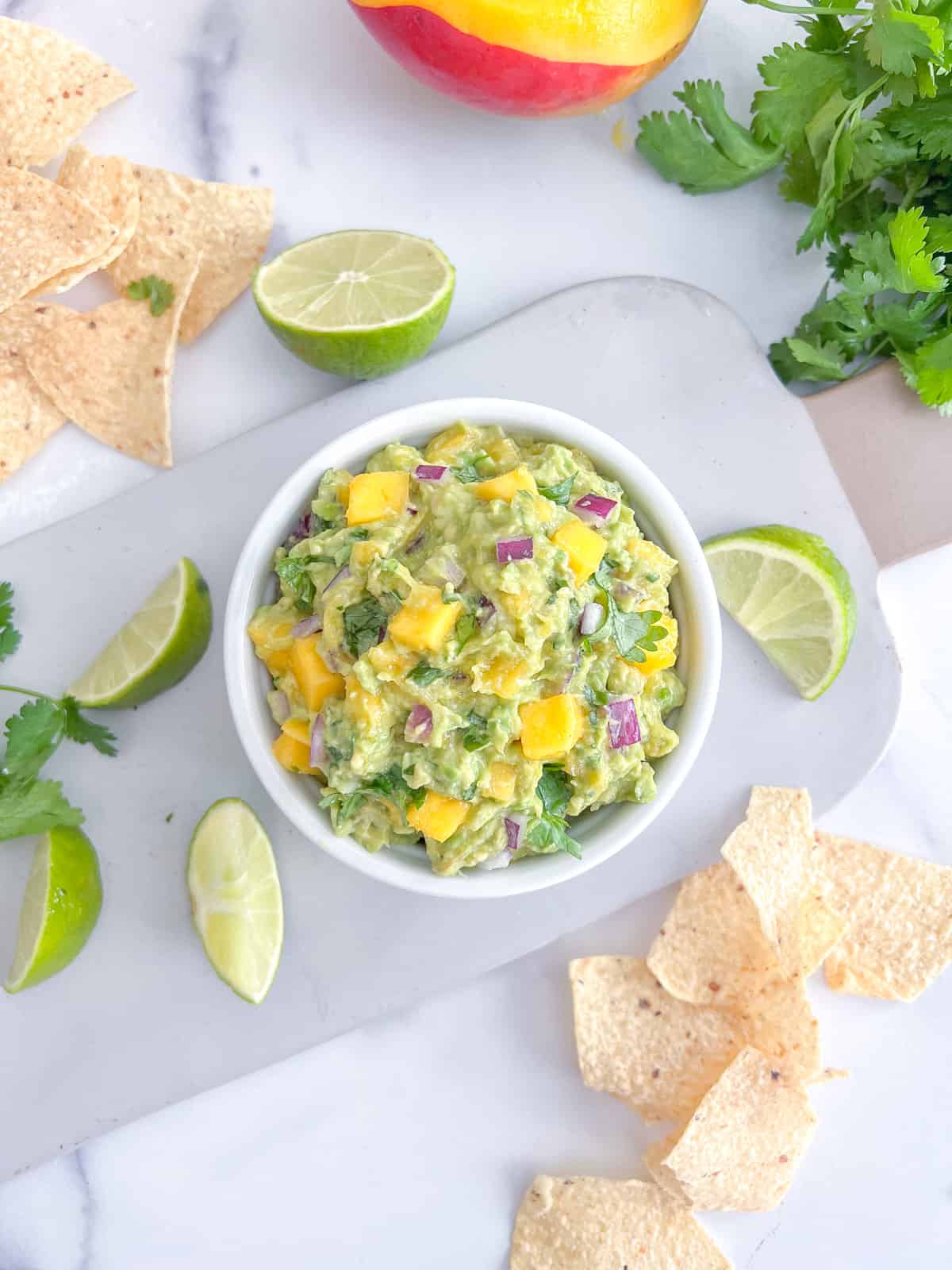 Mango guacamole in a white bowl with chips on the side.