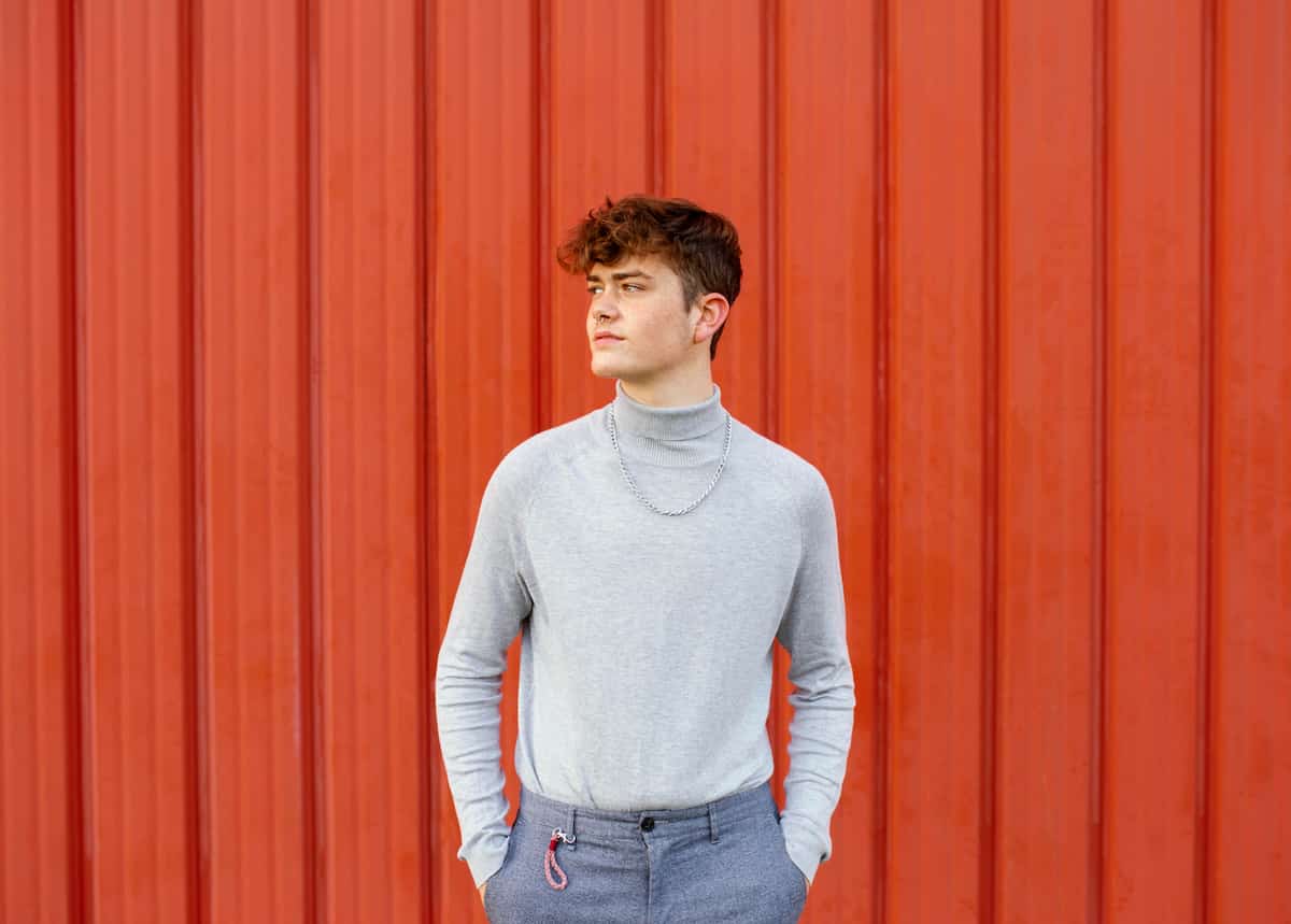 Man in grey turtle neck sweater with large silver chain.