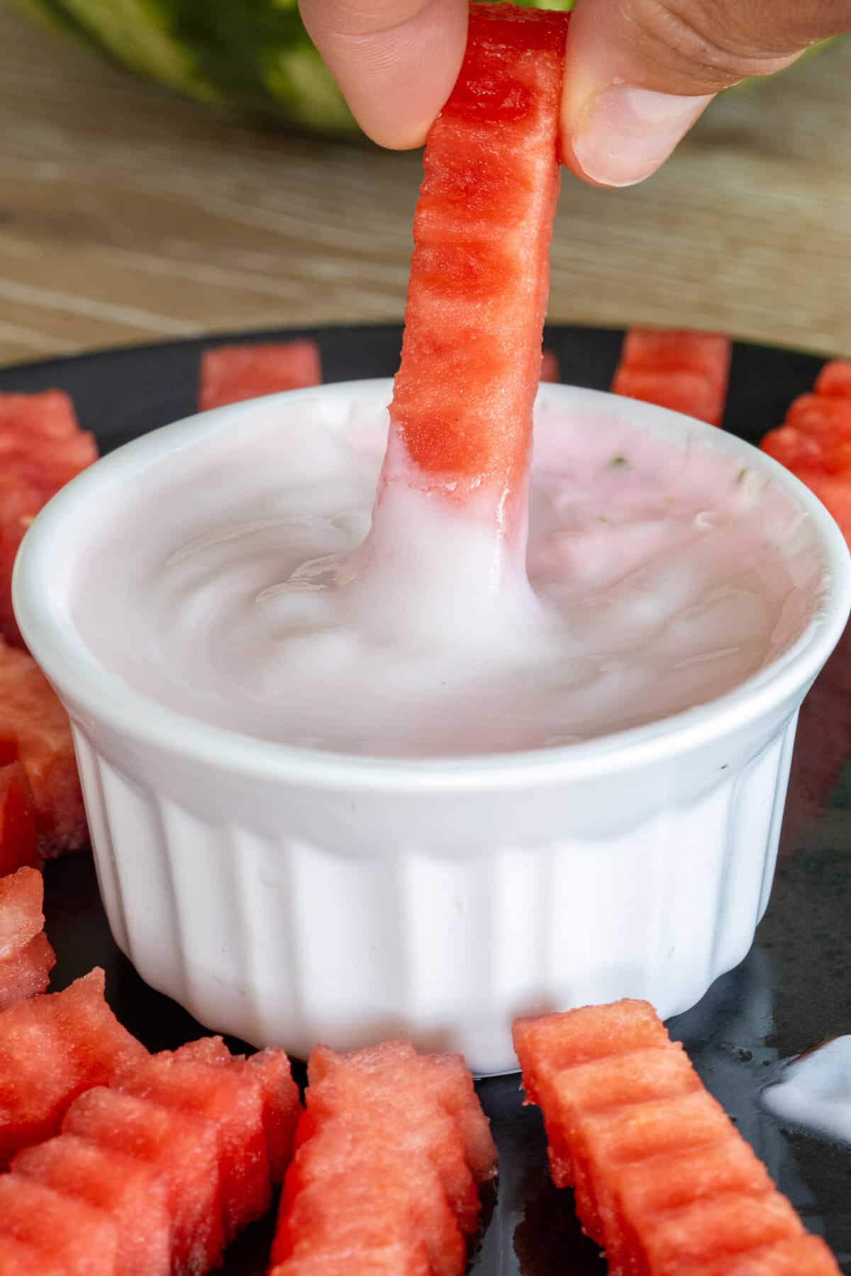 Dipping watermelon stick into yogurt sauce.