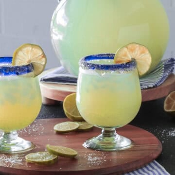 Margarita glasses with lime wedges next to a pitcher.