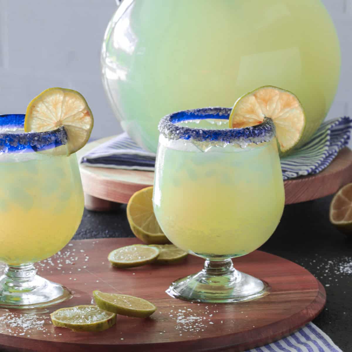 Margarita glasses with lime wedges next to a pitcher.